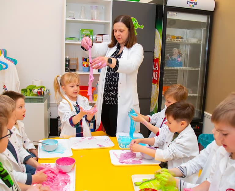 Oktató és gyerekek laborköpenyben slime-ot készítenek